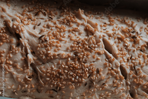 Close-up of unbaked bread dough topped with sesame seeds and cumin seeds.