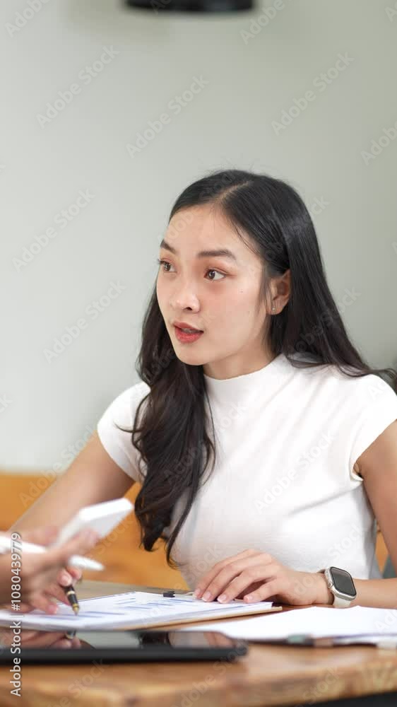 Surprised Woman with Black Hair Takes Notes in White Top During Discussion Surrounded by Papers and Smartphone Surprised Woman with Black Hair Takes Notes in White Top During Discussion Surrounded by Papers and Smartphone