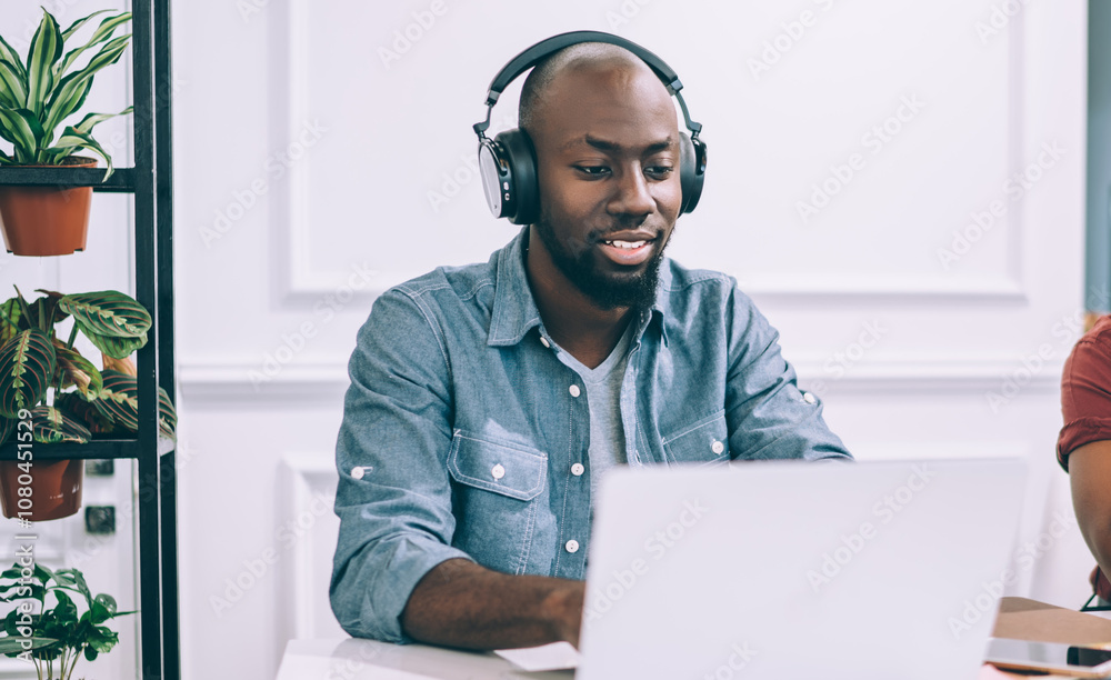 Joyful pensive ethnic man using laptop while sitting at table beside woman talking on phone Joyful pensive ethnic man using laptop while sitting at table beside woman talking on phone