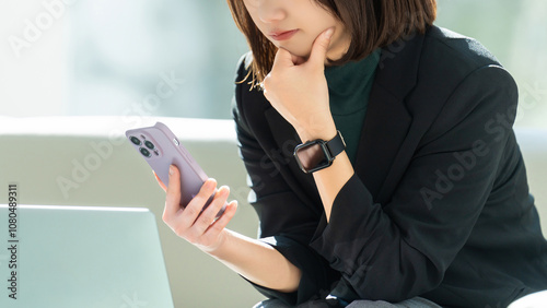 パソコンとスマホを使って真剣な表情で考える女性・ビジネスウーマン