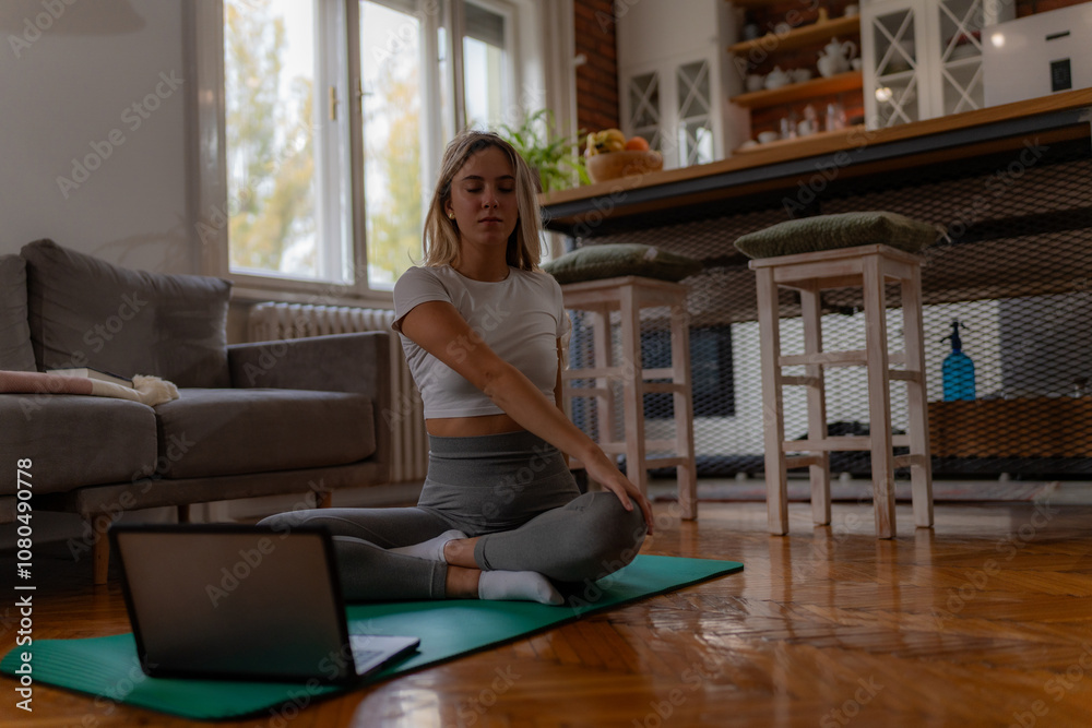 Smiling woman in athletic wear attending virtual yoga session in cozy living room.