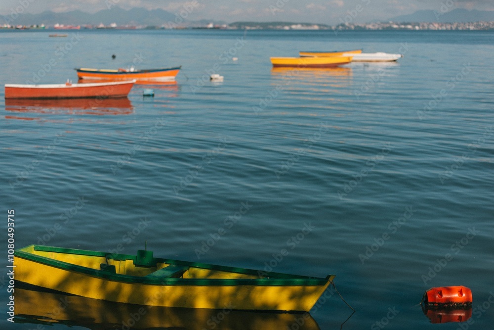Fototapeta premium Colorful boats floating on calm water with distant mountains.