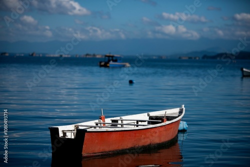 Lone red boat on calm waters with mountain backdrop.