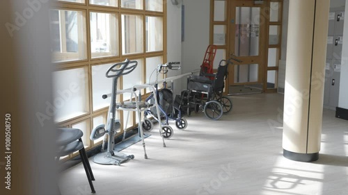 A room with a wheelchair and a walker. The room is empty and the wheelchair is in the middle of the room