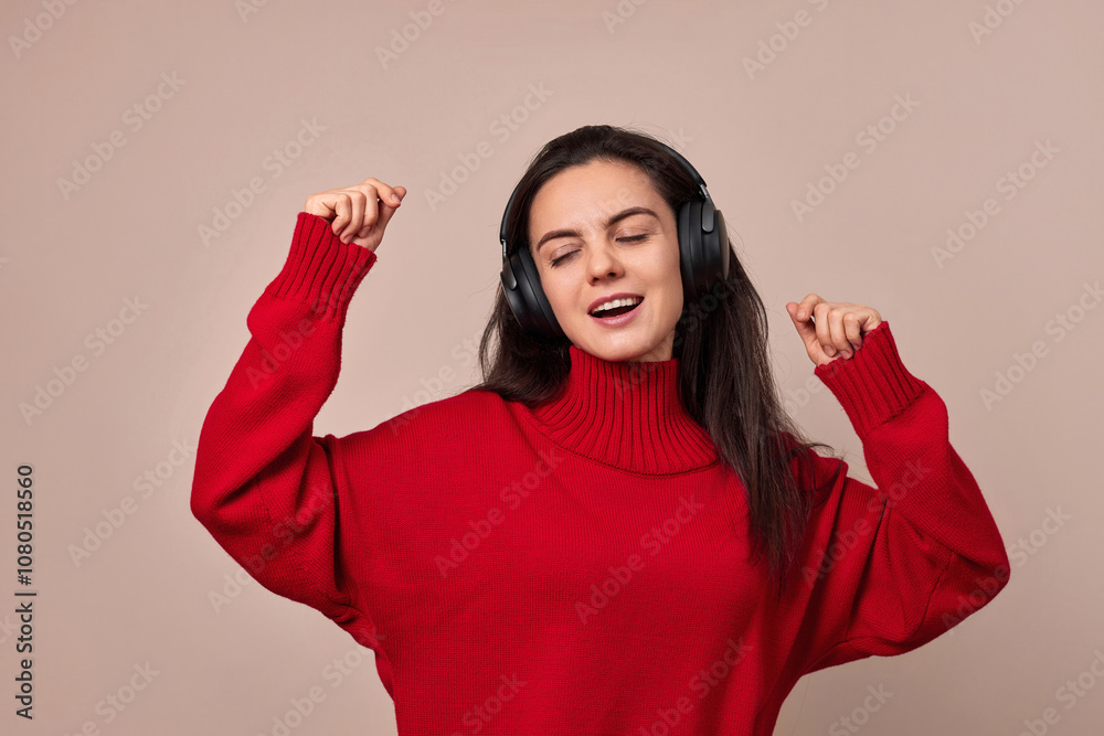 Happy woman wearing red sweater and headphones enjoying listening music and dancing on pink background. Happy woman wearing red sweater and headphones enjoying listening music and dancing on pink background.