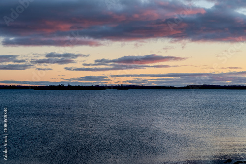 Stunning glowing orange sunset over the serene waters of 1000 Islands, capturing the vibrant colors reflected on the calm surface. Perfect for nature, travel, and scenic stock themes