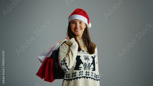 Fun cute woman hold many Christmas shopping bag, gray isolated studio background. Joyful girl buy new year present. Person wear santa claus hat. Lots of gift packages. Ad mock up. Low prices sale eve