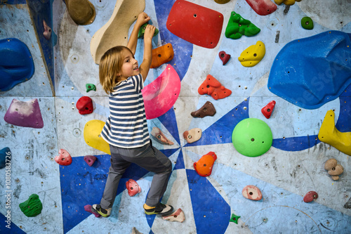 A 6-year-old boy climbing on a vibrant indoor bouldering wall with multicolored holds, engaging in a fun and active climbing experience. Perfect for kids fitness and adventure