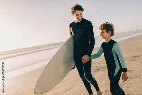 Father and son in wetsuits preparing to surf at the beach