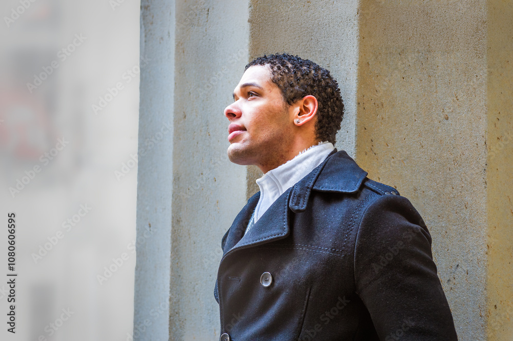 A man in a dark coat gazes upward against a concrete backdrop. Soft lighting highlights his contemplative expression and the texture of his coat.