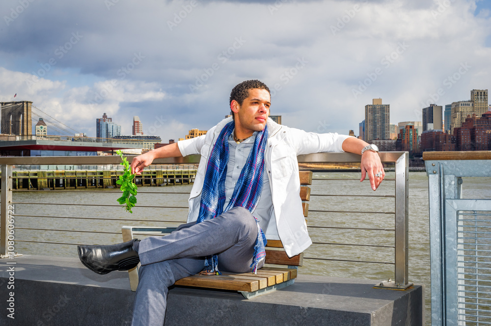 A man dressed stylishly in a white jacket and a blue scarf is seated on a bench by the waterfront, with greenery in hand. The city skyline and a prominent bridge are visible in the background.
