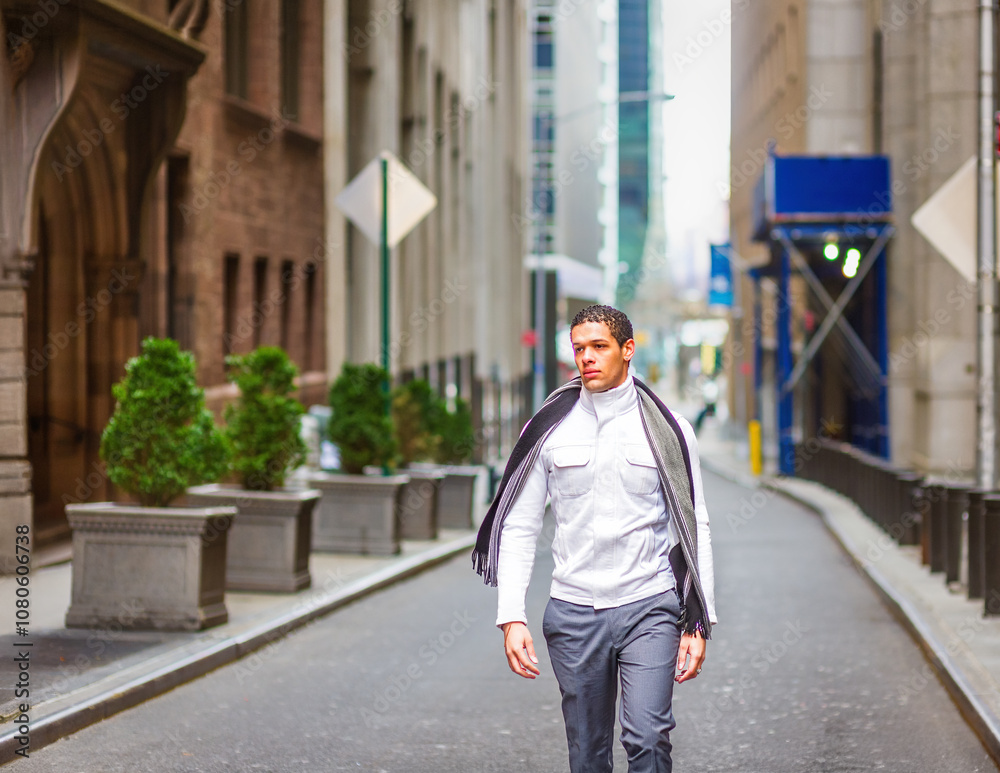A man wearing a scarf and white shirt walks down a narrow city street lined with tall buildings. Potted plants and scaffolding are visible along the sidewalk..