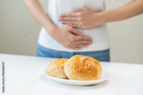 Gluten allergy, asian young woman, girl having a stomach ache hand holding, refusing to eat white loaf slice on plate in breakfast food meal at home. Gluten intolerant and Gluten free diet concept. photo