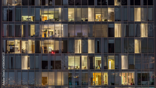 Windows of the multi-storey building of glass and steel lighting inside and moving people within timelapse