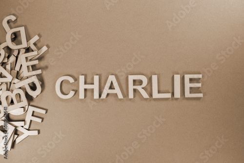 Popular and modern baby girl fashion name CHARLIE in wooden English language capital letters spilling from a pile of letters on a purple background in sepia