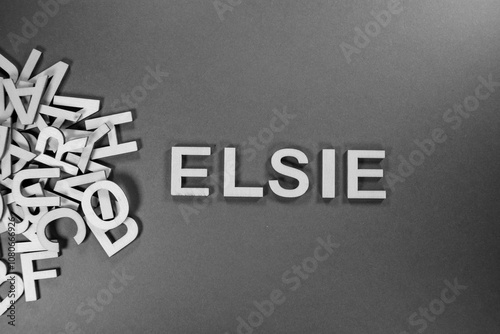 Popular and modern baby girl fashion name ELSIE in wooden English language capital letters spilling from a pile of letters on a red background in black and white photo