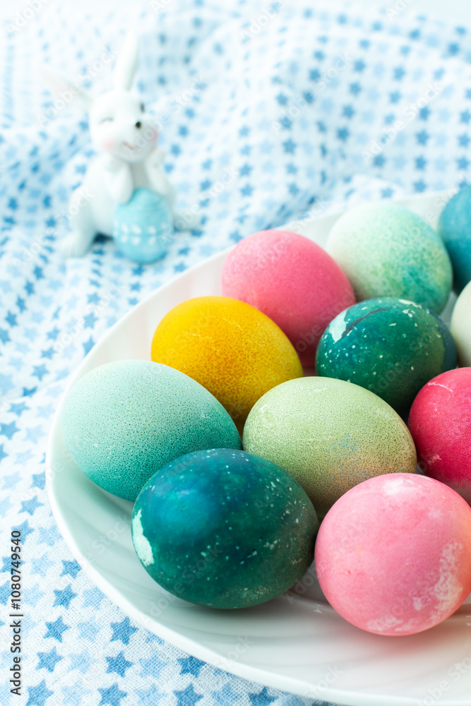 Multi-colored Easter eggs in an oval dish with decorative bunnies on a blue tablecloth, Happy Easter holiday Multi-colored Easter eggs in an oval dish with decorative bunnies on a blue tablecloth, Happy Easter holiday