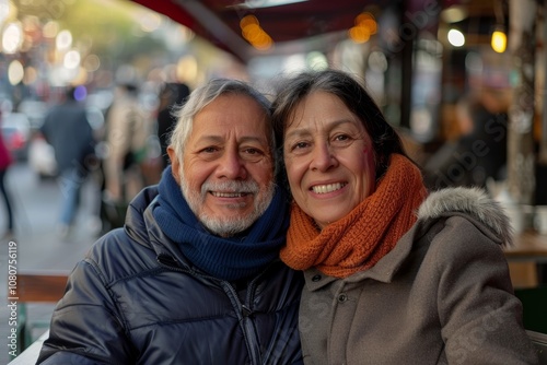 Portrait of a jovial latino couple in their 50s wearing a protective neck gaiter in front of bustling city cafe