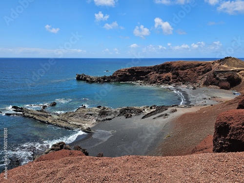 La côte rocheuse d’El Golfo s’étend sous un ciel dégagé, où le bleu profond de l’océan Atlantique contraste avec les teintes volcaniques des falaises et du sable noir, offrant un paysage sauvage. photo