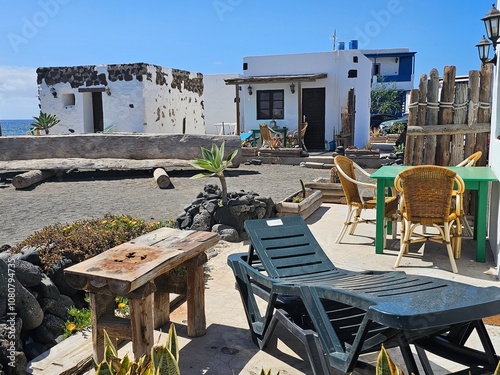 Un petit coin de détente rustique et charmant avec des chaises en osier, des tables en bois brut et des murs blanchis à la chaux, capturant l’ambiance paisible et authentique du bord de mer à El Golfo photo