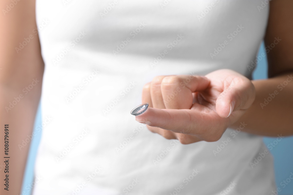 Woman holding color contact lens on light blue background, closeup Woman holding color contact lens on light blue background, closeup