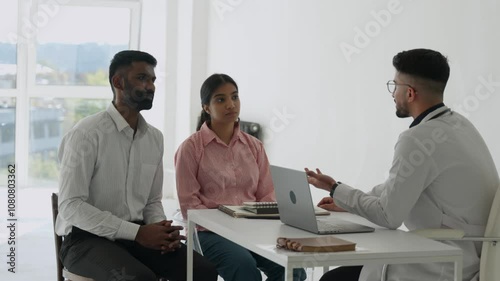 Portrait of a young happy indian asian couple talking with a male friendly family doctor therapist in medical clinic or hospital planning pregnancy. Health care and check up concept