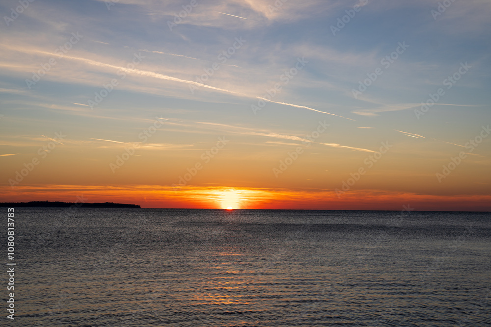 Naklejka premium Piran, Slovenia - November 3, 2024: Sunset against the backdrop of a calm sea. The sun goes down behind the sea horizon.