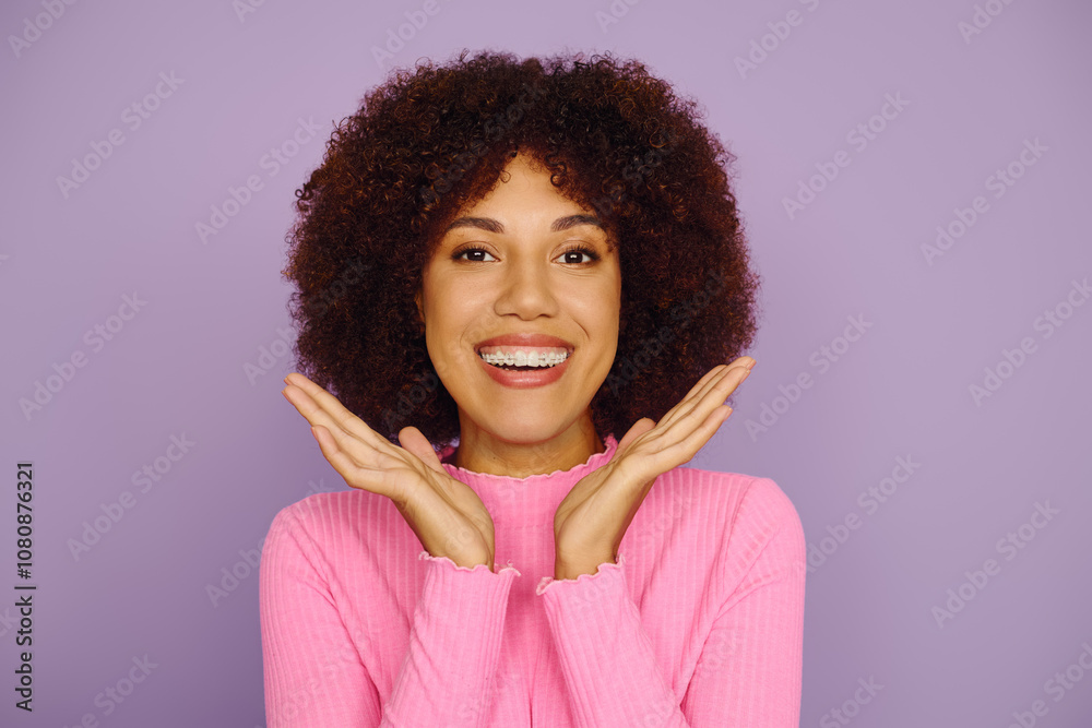 A young African American woman beams with joy, showcasing her curly hair while dressed in casual pink clothing. A young African American woman beams with joy, showcasing her curly hair while dressed in casual pink clothing.
