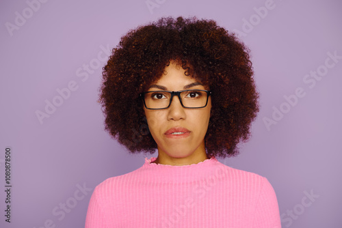 A young African American woman in pink clothing and glasses while standing on a purple backdrop.