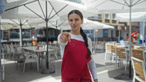 Woman pointing in a cafe terrace with outdoor seating under umbrellas on a sunny day, showing a playful interaction.