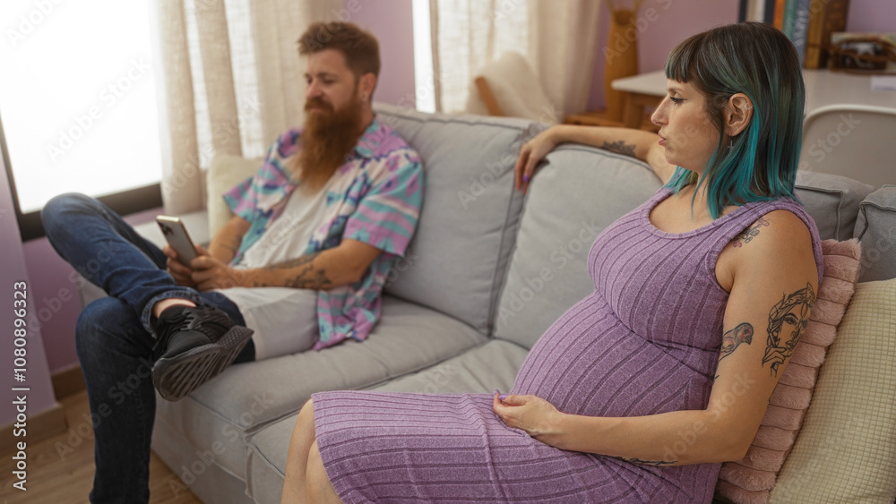 Pregnant woman with tattoos sitting on a couch in a living room while a bearded man next to her looks at his phone, showcasing a contemporary family moment indoors. Pregnant woman with tattoos sitting on a couch in a living room while a bearded man next to her looks at his phone, showcasing a contemporary family moment indoors.