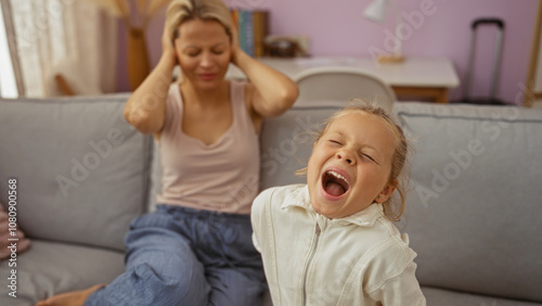 Woman with blonde hair stressed as daughter screams in indoor home living room