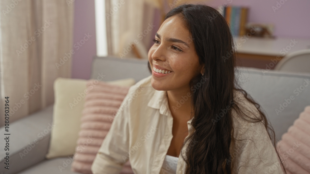 Beautiful young hispanic woman smiling indoors in a cozy living room, showcasing her long brunette hair and warm, modern home environment. Beautiful young hispanic woman smiling indoors in a cozy living room, showcasing her long brunette hair and warm, modern home environment.