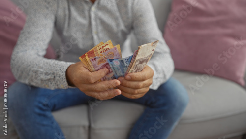 Hispanic man counting mexican pesos indoors in a living room