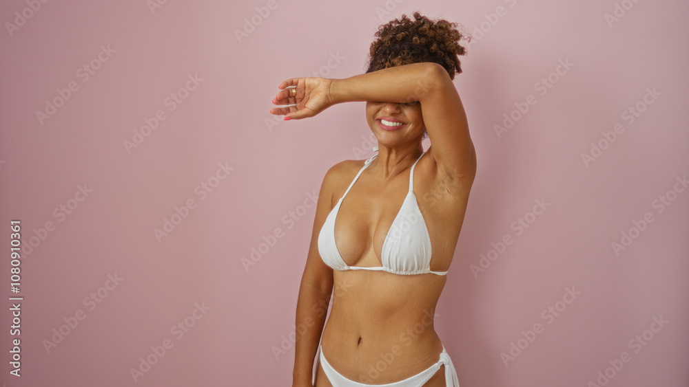 Naklejka premium Young woman in white bikini posing against an isolated pink background with her arm covering her face showing happy and relaxed expression