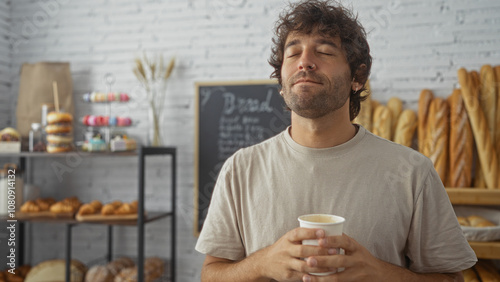 Handsome young man enjoying coffee inside a bakery with fresh bread and pastries in the background