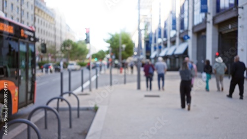 Defocused people strolling along a bustling street in marseilles under clear skies, creating a vibrant urban atmosphere with blurred movement and modern architecture.