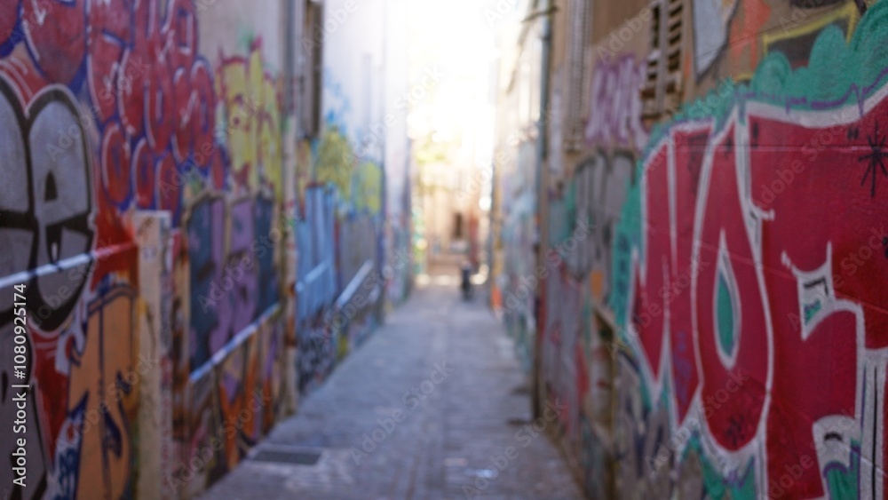 Fototapeta premium Blurred view of graffiti-covered alleyway suggests urban street art scene with vibrant colors, emphasizing defocused backgrounds typical of ghetto culture.
