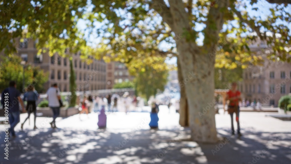 Blurred scene of people walking on a sunny street in marseilles, france with trees in the foreground creating a bokeh effect. Blurred scene of people walking on a sunny street in marseilles, france with trees in the foreground creating a bokeh effect.
