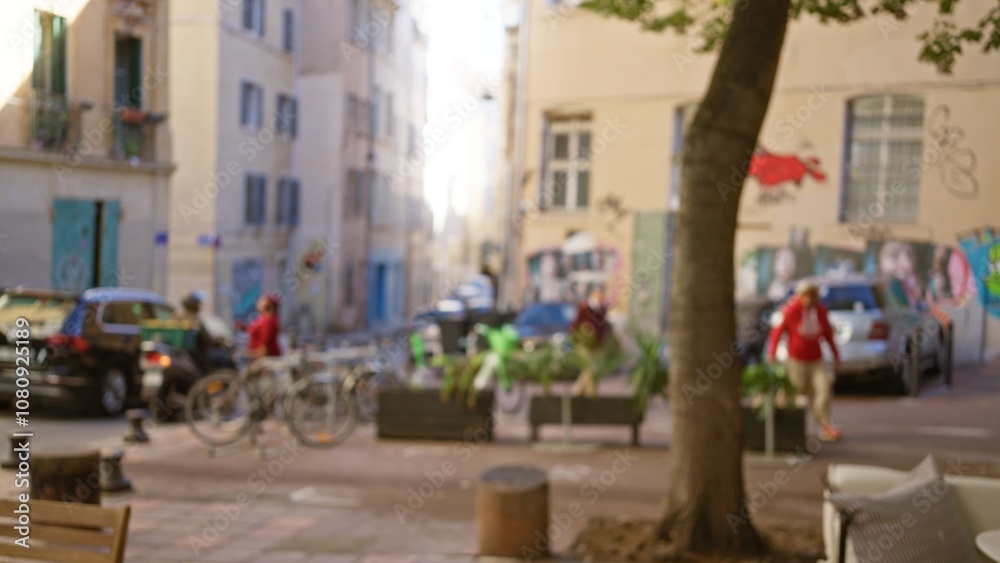 Fototapeta premium Blurred street in marseilles with defocused people and parked cars under soft daylight highlighting urban charm and european atmosphere.