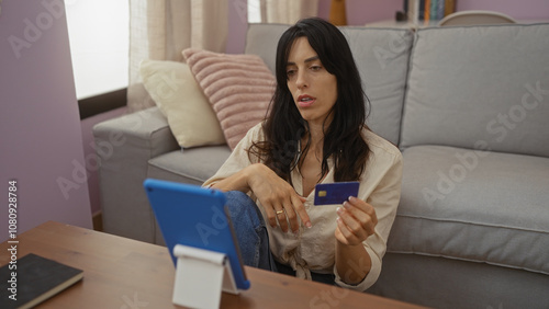 Woman shopping online using tablet holding credit card while sitting in living room at home