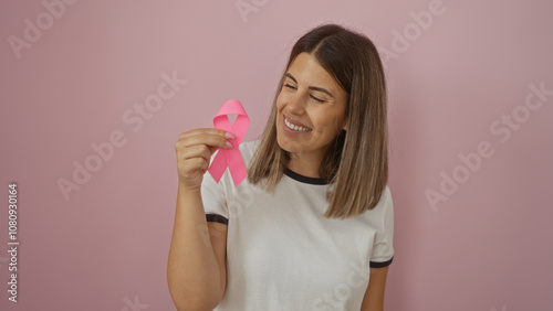 Young woman holding a pink breast cancer awareness ribbon, smiling warmly, isolated against a pink background