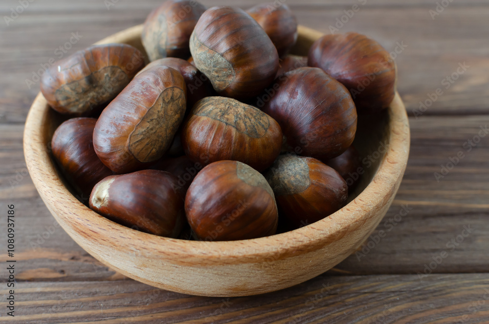 Edible raw chestnuts in a wooden bowl on the table. The concept of autumn food. Street food. Selective focus. Horizontal orientation. Edible raw chestnuts in a wooden bowl on the table. The concept of autumn food. Street food. Selective focus. Horizontal orientation.