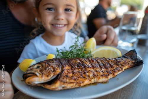 A cheerful child displays a freshly grilled fish garnished with herbs and lemon on a plate, capturing a moment of joyous mealtime in a bright, lively setting.