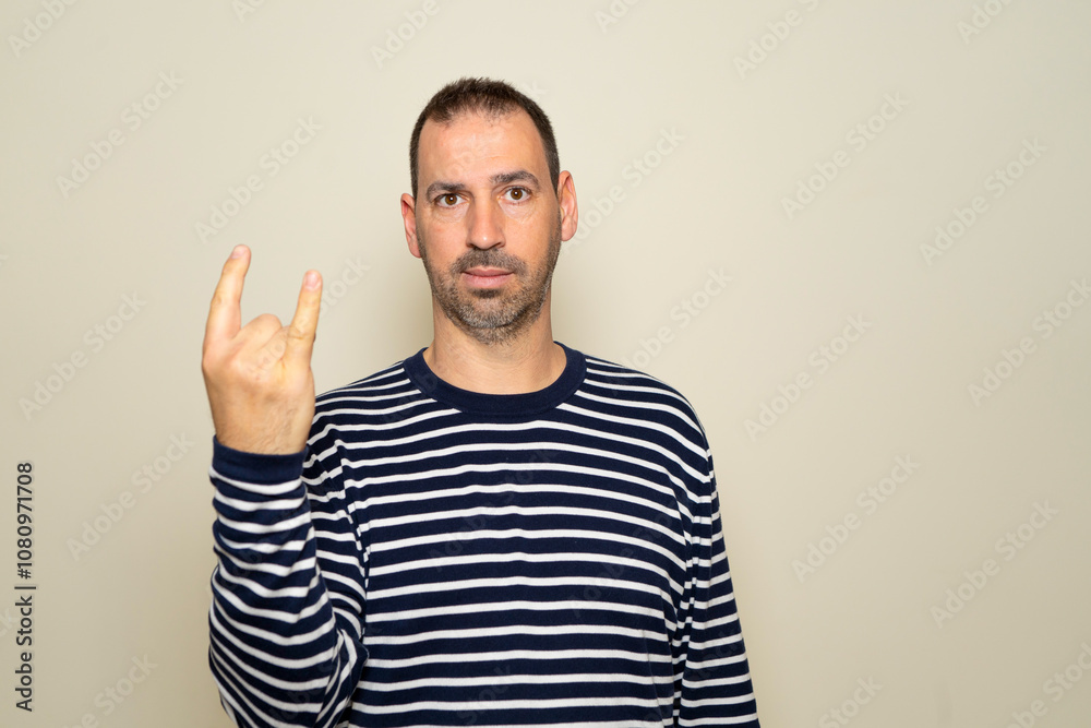 Portrait of bearded man showing rock and roll gesture, heavy metal sign, exclaiming with joy. Indoor studio photo isolated on beige background. Portrait of bearded man showing rock and roll gesture, heavy metal sign, exclaiming with joy. Indoor studio photo isolated on beige background.