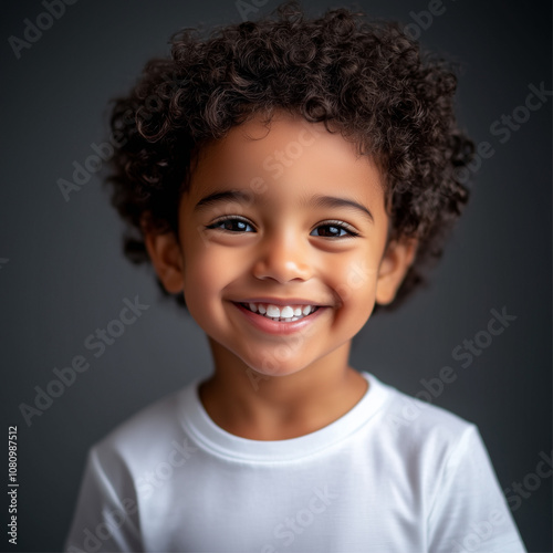 A joyful young child with curly hair dressed in white smiles happily.