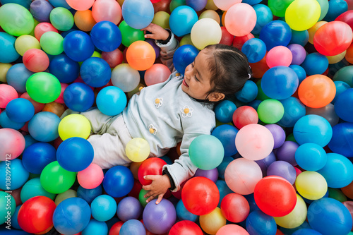 Little latina girl plays in a colorful ball pool