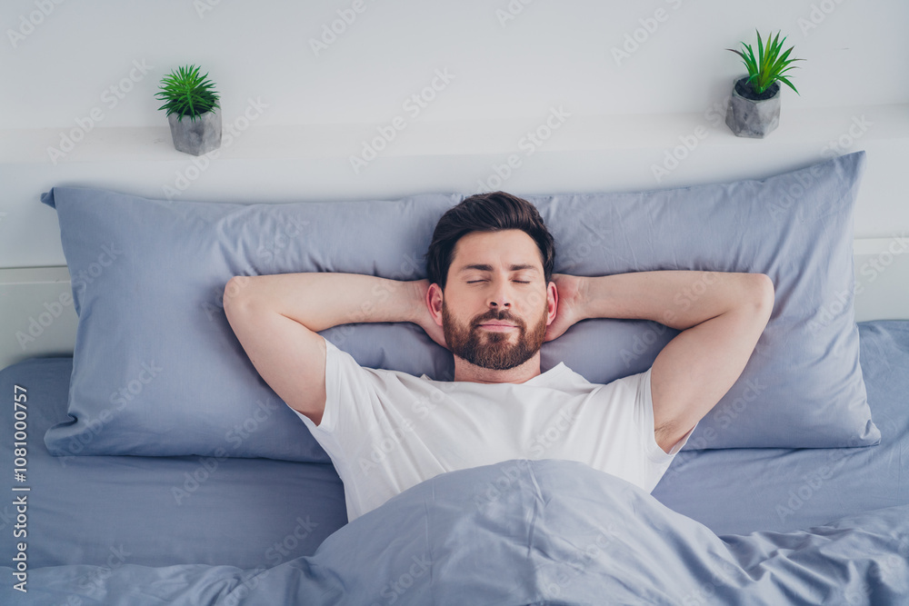 Photo of attractive funny young man nightwear pajama lying bed arms behind head indoors house apartment room Photo of attractive funny young man nightwear pajama lying bed arms behind head indoors house apartment room