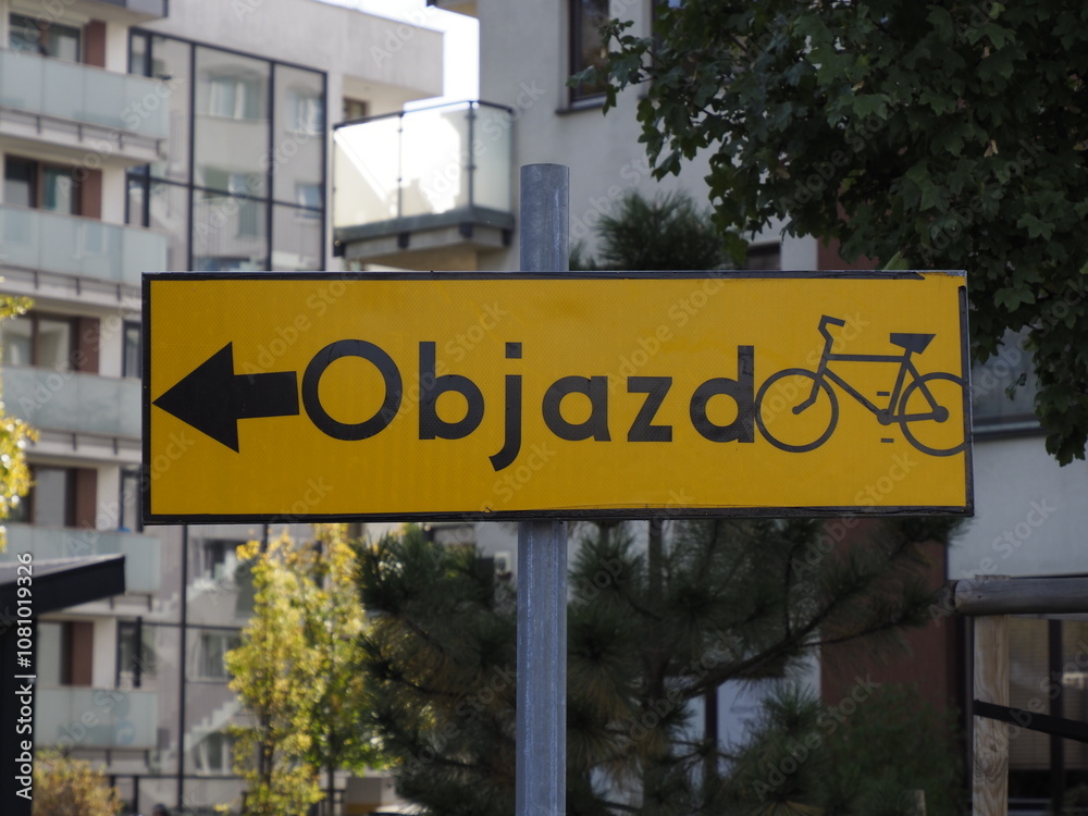 Obraz premium Yellow detour road sign for cyclists against urban architecture background