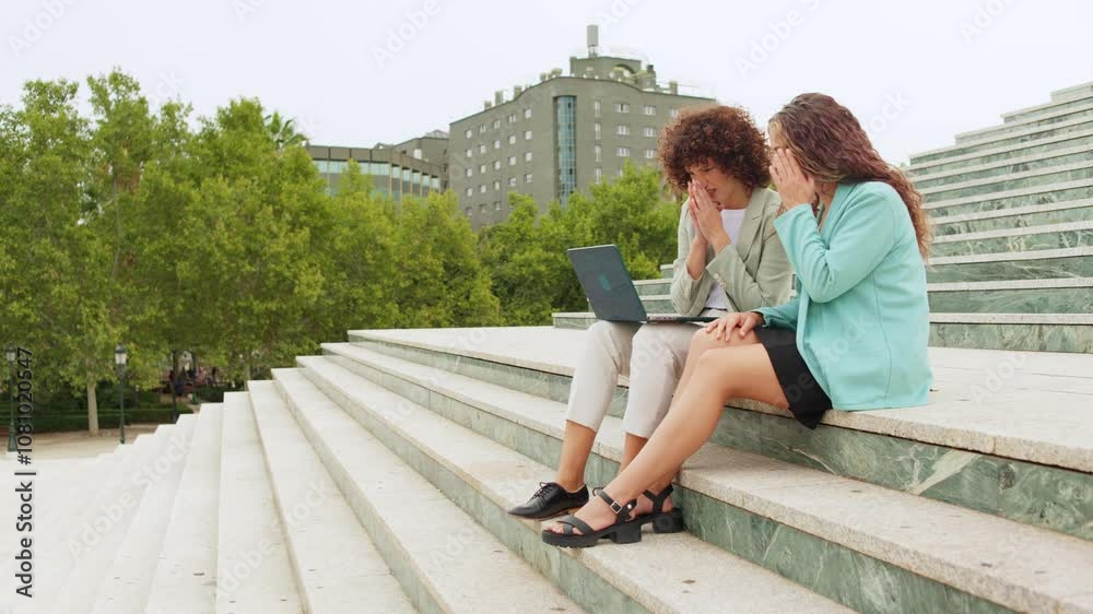 Businesswomen reacting to unexpected news on laptop outdoors Businesswomen reacting to unexpected news on laptop outdoors